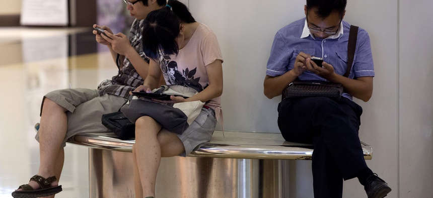 People sit on a bench inside a shopping mall using their tablet computer and smartphone in Beijing, China Monday, Aug. 19, 2013.
