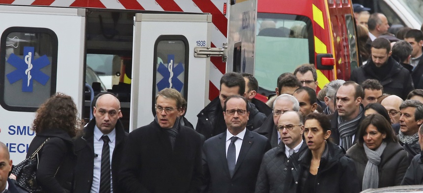 French President Francois Hollande, center, flanked with security forces gestures, as he arrives outside the French satirical newspaper Charlie Hebdo's office, in Paris, Wednesday, Jan 7th
