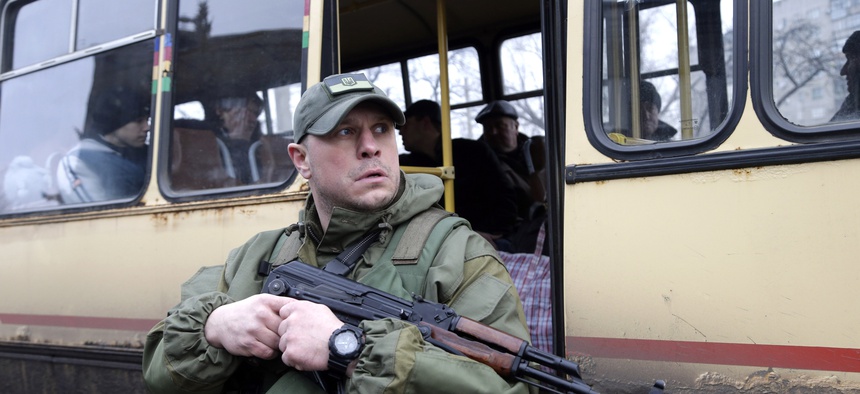 A Ukrainian soldier holds a weapon as people wait on a bus to leave the town of Debaltseve in Artemivsk, Ukraine, on February 3, 2015.