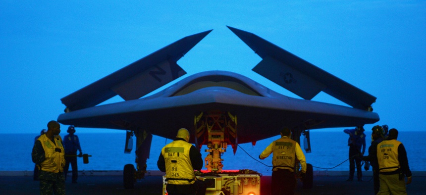 An X-47B Unmanned Combat Air System (UCAS) demonstrator is towed into the hangar bay of the aircraft carrier USS George H.W. Bush.