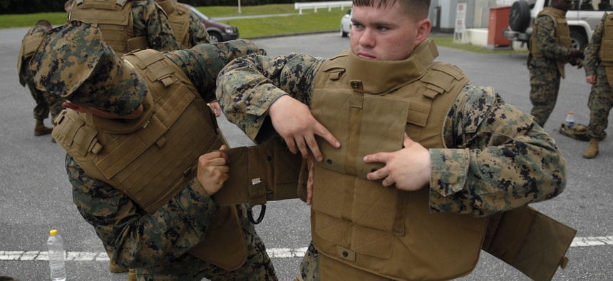 Marines with the 3rd Marine Logistics Group help each other configure their new Modular Tactical Vests before vest trainers inspect individual Marines for proper fit.