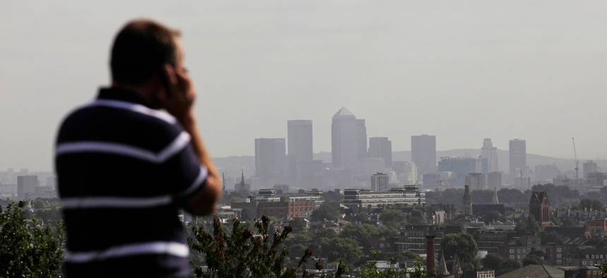 A man talks on a mobile phone as the hi-rise buildings of the banks based in the Canary Wharf business district are seen in the distance from Parliament Hill on Hampstead Heath in London, Sept. 23, 2011.