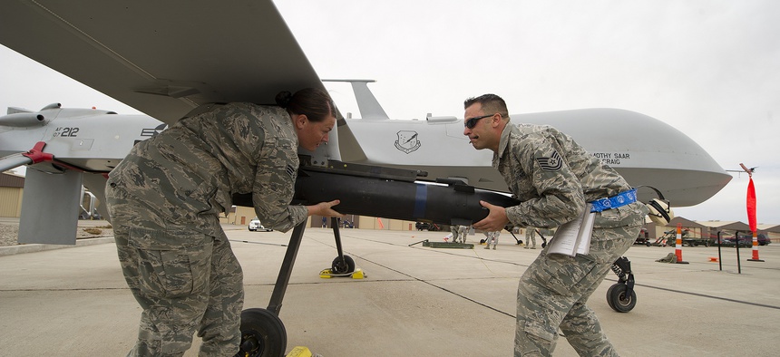 Two Air Force NCOs load munitions on an MQ-9 Predator.