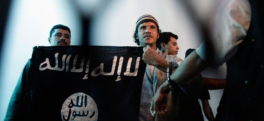 In this April 23, 2013 file photo, a suspected Yemeni al-Qaida militant, center, holds a banner as he stands behind bars during a court hearing in state security court in Sanaa, Yemen.