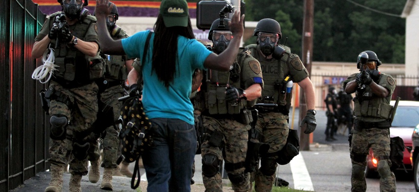 In this Aug. 11, 2014 photo, police wearing riot gear point their weapons before arresting a man in Ferguson, Mo.