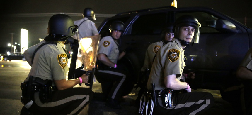 Police take cover behind a vehicle during a protest in Ferguson, Mo., Sunday, Aug. 9, 2015.