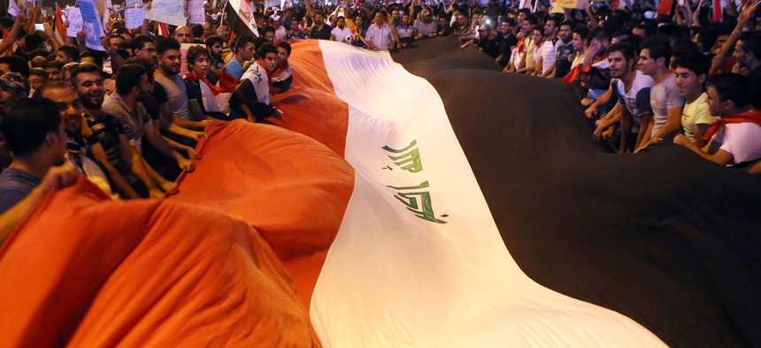 Protesters chant in support of Iraqi Prime Minister Haider al-Abadi as they carry a large national flag during a demonstration in Tahrir Square in Baghdad, Iraq, Friday, Aug. 14, 2015.