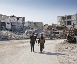 In this Wednesday, Nov. 19, 2014 photo, Kurdish People's Protection Units (YPG) soldiers walk near the town entrance circle heading to their strongholds in Kobani, Syria. In this Wednesday, Nov. 19, 2014 photo, Kurdish People's Protection Units (YPG) soldiers walk near the town entrance circle heading to their strongholds in Kobani, Syria.