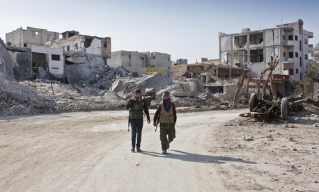 In this Wednesday, Nov. 19, 2014 photo, Kurdish People's Protection Units (YPG) soldiers walk near the town entrance circle heading to their strongholds in Kobani, Syria. In this Wednesday, Nov. 19, 2014 photo, Kurdish People's Protection Units (YPG) soldiers walk near the town entrance circle heading to their strongholds in Kobani, Syria.