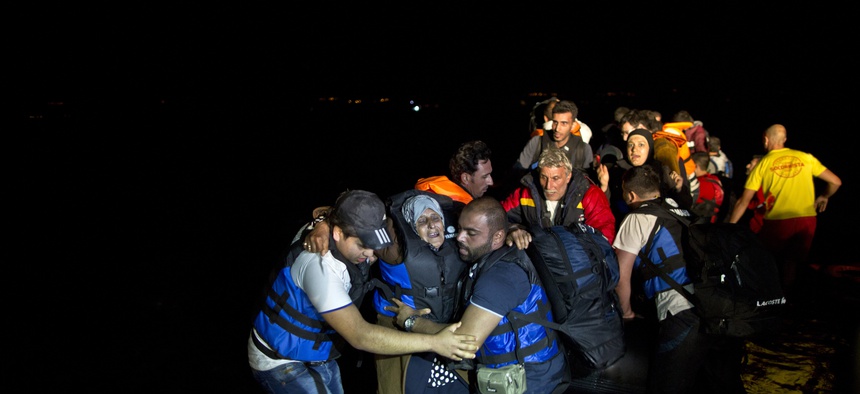 Two Syrian refugees try to carry an elderly woman off a dinghy as it arrives from the Turkish coast to the northeastern Greek island of Lesbos, Tuesday, Oct. 6 , 2015.