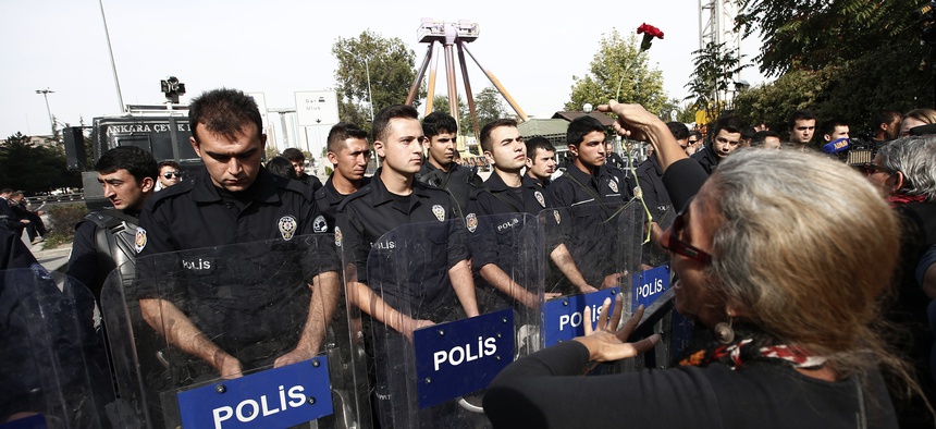 A protester throws carnations to Turkish police blocking the way to the site of Saturday's explosions in Ankara, Turkey, Sunday, Oct. 11, 2015. Scuffles broke out as police prevented pro-Kurdish politicians and other mourners from laying carnations at the