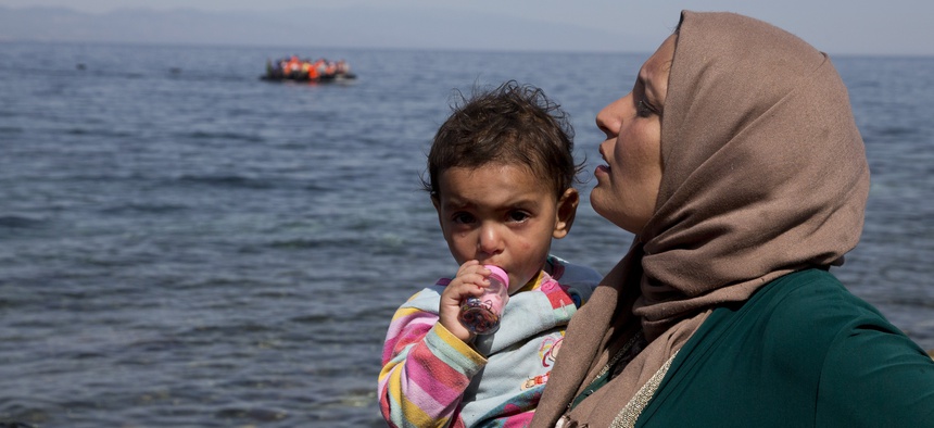 A dinghy full of migrants approaches the coast of the Greek island of Lesbos after crossing from Turkey to Greece as a Syrian woman who just arrive holds her child,Thursday, Sept. 10, 2015.