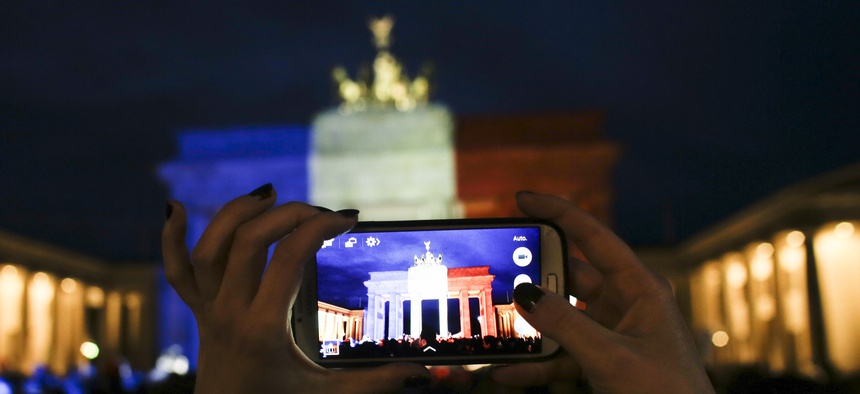 A woman takes a picture of the Brandenburg Gate, illuminated in the French national colors for the victims killed in the Friday's attacks in Paris, France in Berlin, Saturday, Nov. 14, 2015.