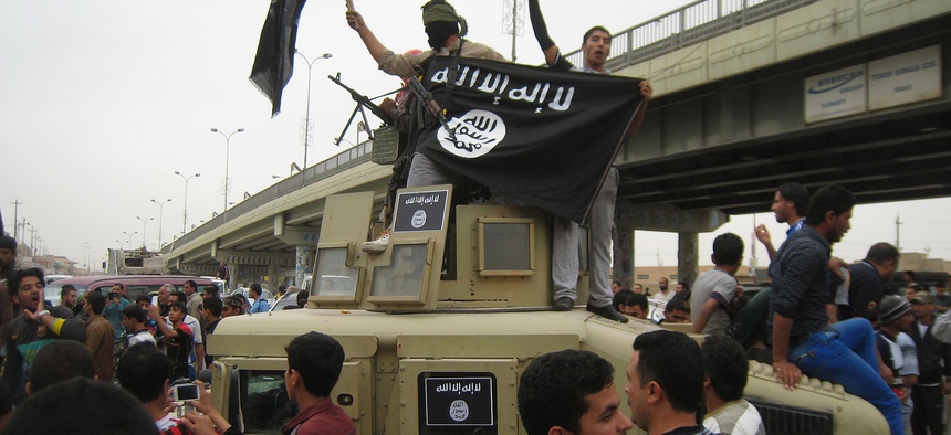 In this Sunday, March 30, 2014, file photo, Islamic State group militants hold up their flag as they patrol in a commandeered Iraqi military vehicle in Fallujah.