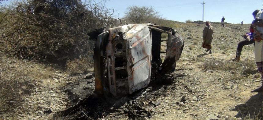 People gather near a destroyed car that was carrying militants in the Sawmaa area of al-Bayda province, Yemen, Saturday, April 19, 2014.
