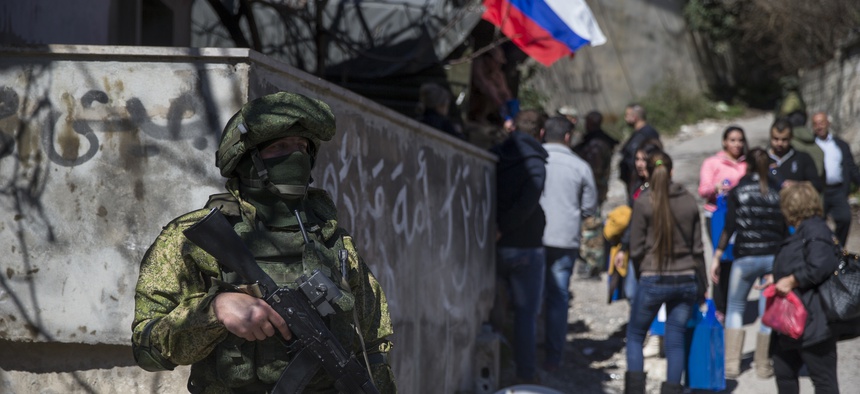 A Russian soldier keeps watch as local residents receive humanitarian aid in the Syrian village of Ghunaymiyah, about 15 kilometers from Turkish border, Tuesday, March 1, 2016.