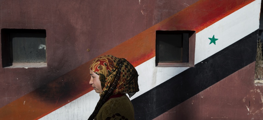In this Thursday, March 3, 2016 photo, a woman passes a painting of Syrian flag in At-Tall, a town of northern outskirts of Damascus, Syria.