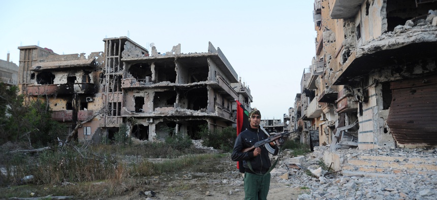 n this Feb. 23, 2016 file photo, a civilian fighter holding the Libyan flag stands in front of damaged buildings in Benghazi, Libya. The U.S., Europe and U.N. have all pinned their hopes for resolving Libya’s chaos and blocking the Islamic State group’s g