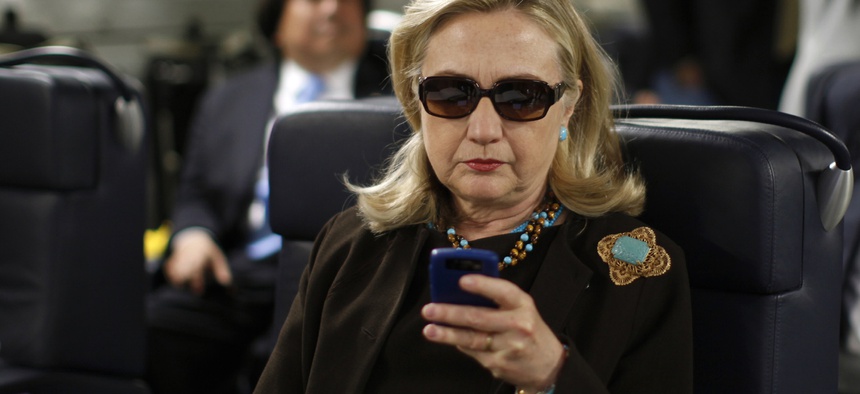 In this Oct. 18, 2011, file photo, then-Secretary of State Hillary Rodham Clinton checks her Blackberry from a desk inside a C-17 military plane upon her departure from Malta, in the Mediterranean Sea, bound for Tripoli, Libya.