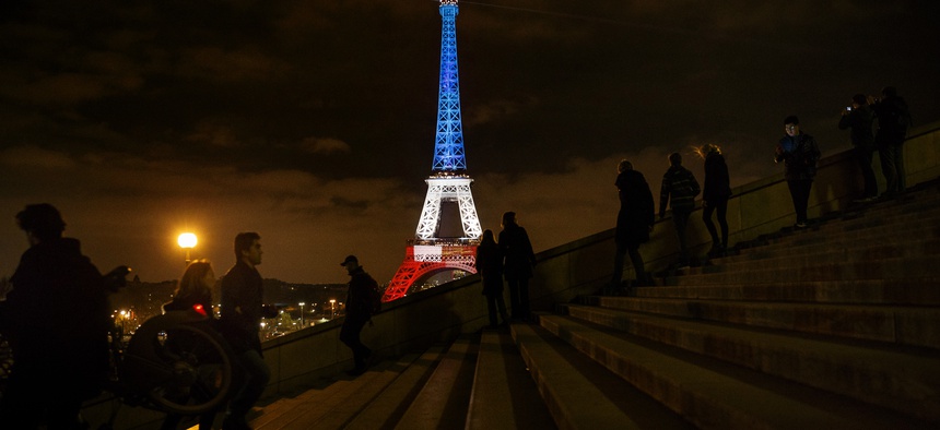 People walk and take pictures in front of the Eiffel Tower illuminated in the French colors in honor of the victims of the attacks on Friday in Paris, Monday, Nov. 16, 2015.