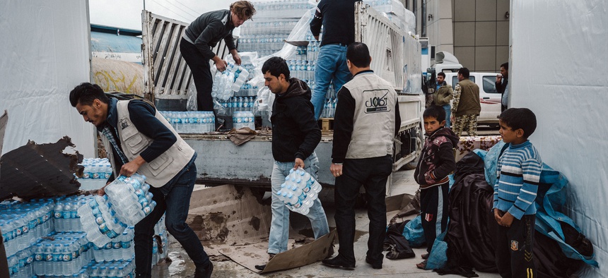 Men help unload a supply of mineral water for displaced civilians at a shelter in Makhmour, east of Mosul, Iraq, on March 28, 2016.