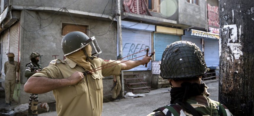 An Indian policeman uses a sling to shoot glass marbles at Kashmiri protesters during a protest in Srinagar, Indian controlled Kashmir, Friday, Oct. 7, 2016.