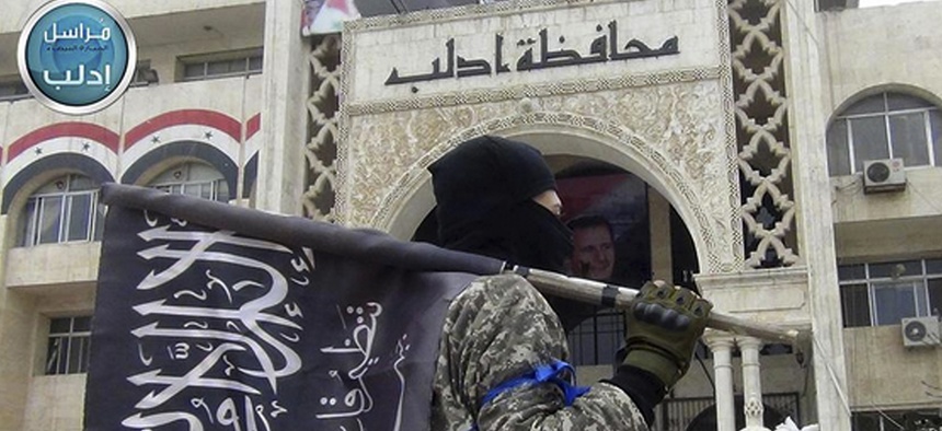 A fighter from Syria's al-Qaida-linked Nusra Front holds his group flag as he stands in front of the governor building in Idlib province, north Syria, March 28, 2015.