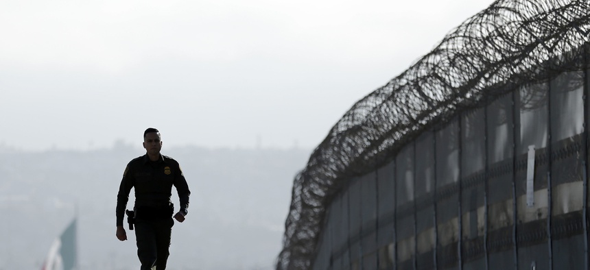 Border Patrol agent Eduardo Olmos walks near the secondary fence separating Tijuana, Mexico, background, and San Diego in San Diego, June 22, 2016.