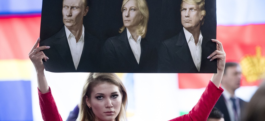 In this Dec. 23, 2016 file photo, a journalist holds a poster with portraits of Russian President Vladimir Putin, left, France's far-right National Front president, Marine Le Pen, center, and President-elect Donald Trump, prior to Putin's annual pr event.