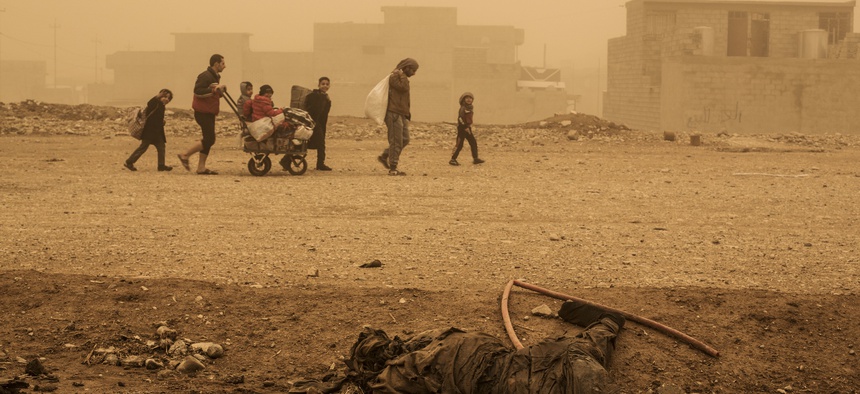 A group of civilians pass close to the body of an Islamic State militant, while fleeing from Mosul due to ISIS heavy shelling in several areas under control of the Iraqi Army, Mosul, Iraq, Friday, Dec. 2, 2016.