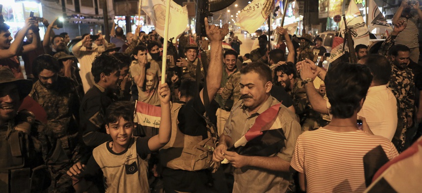 Iraqi security and civilians celebrate while holding national flags as they wait for the final announcement of the defeat of the Islamic state militants, in Basra, 340 miles (550 kilometers) southeast of Baghdad, Iraq, Sunday, July 9, 2017.
