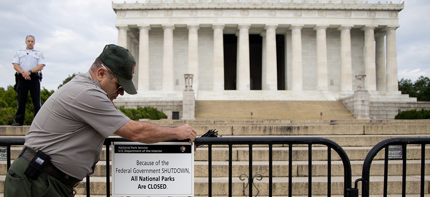 A U.S. Park Police officer watches at left as a National Park Service employee posts a sign on a barricade closing access to the Lincoln Memorial in Washington.