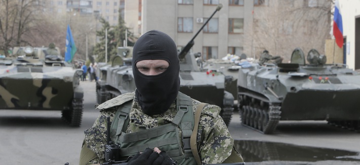 A masked gunman guards combat vehicles with Russian, Donetsk Republic and Ukrainian paratroopers, flags and gunmen on top, parked in downtown of Slovyansk on Wednesday, April 16, 2014. 