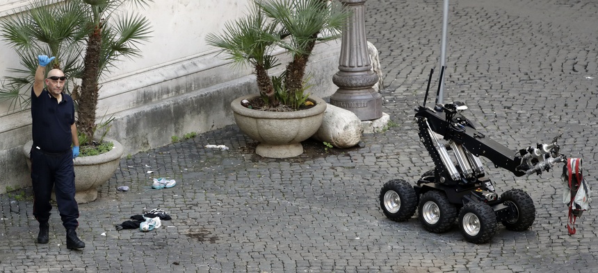 An Italian Carabinieri explosive expert gives the thumbs up sign near a bomb disposal robot after it detonated an unattended bag near Grazioli palace, former Italian Premier Silvio Berlusconi residency, in Rome, Oct. 8, 2016.
