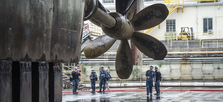 Sailors assigned to the submarine tender USS Frank Cable (AS 40) see their ship's propeller for the first time, as she drains in dry-dock, in Portland, Ore.