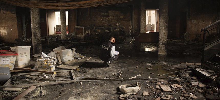 A police officer investigates damages at Libya's high national elections commission in Tripoli after a suicide bombing Wednesday, May 2, 2018.