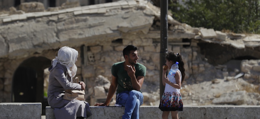 In this photo taken on Thursday, Aug. 16, 2018, Syrians sit in the square in the city of Aleppo, Syria.