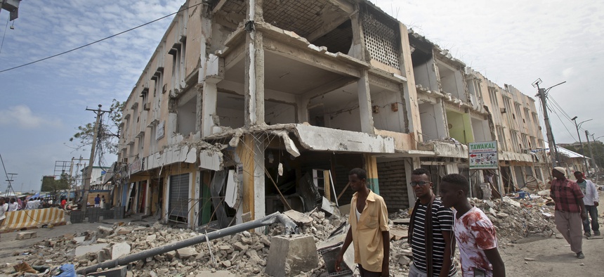 Men walk near destroyed buildings as thousands of Somalis gathered to pray at the site of the country's deadliest attack and to mourn the hundreds of victims, at the site of the attack in Mogadishu, Somalia Friday, Oct. 20, 2017.