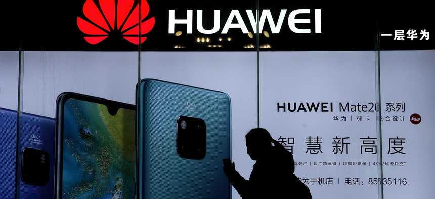 A woman browses her smartphone as she walks by a Huawei store at a shopping mall in Beijing, Tuesday, Dec. 11, 2018.
