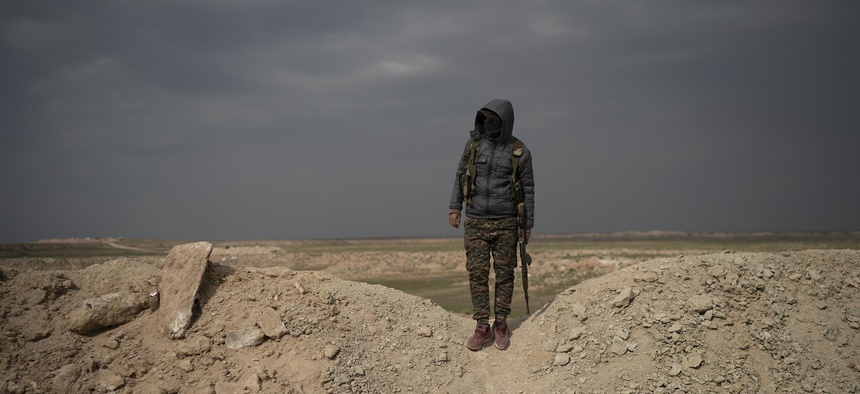 A U.S.-backed Syrian Democratic Forces, or SDF, fighter stands in the desert outside the village of Baghouz, Syria, Thurs., Feb. 14, 2019.