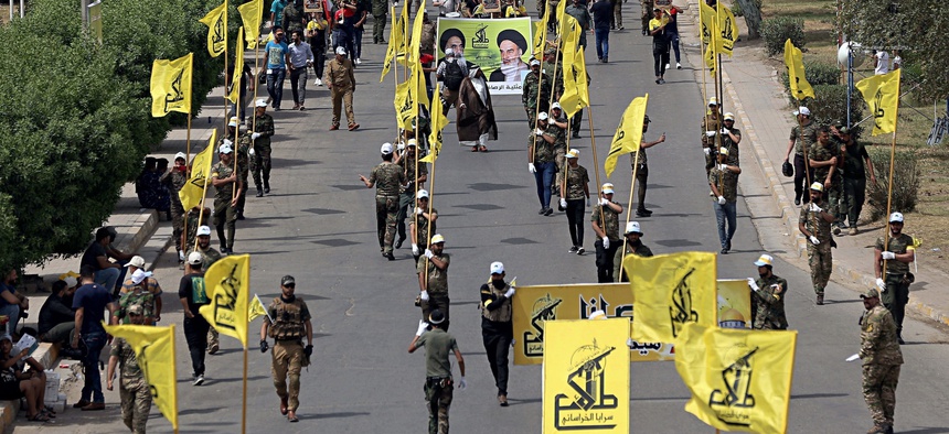 In this June 8, 2018 file photo, Iraqi Popular Mobilization Forces march as they hold their flag and posters of Iraqi and Iranian Shiites spiritual leaders during "al-Quds" or Jerusalem Day, in Baghdad, Iraq.