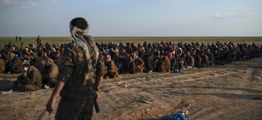 In this Feb. 22, 2019 file photo, U.S.-backed Syrian Democratic Forces (SDF) fighters stand guard next to men waiting to be screened after being evacuated out of the last territory held by Islamic State group militants, near Baghouz, eastern Syria.