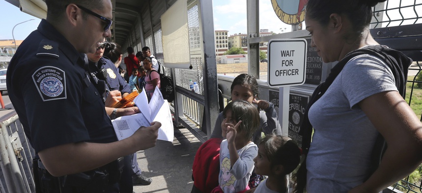 A United States Customs and Border Protection Officer checks the documents of migrants, before being taken to apply for asylum in the United States, on the International Bridge 1 in Nuevo Laredo, Mexico, Wednesday, July 17, 2019.