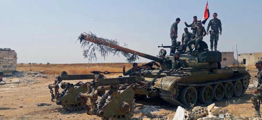 In this Tuesday, Aug. 13, 2019 photo, released by the Syrian official news agency SANA, Syrian army soldiers flash the victory sign as they stand on a tank, in northwestern Syria.