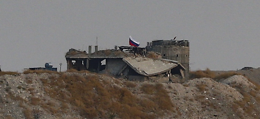 In this photo taken from the Turkish side of the border between Turkey and Syria, in Karkamis, Gaziantep province, southeastern Turkey, a Russian flag is hoisted on a damaged building near the Syrian town of Zor Mahar, Thursday, Oct. 17, 2019.