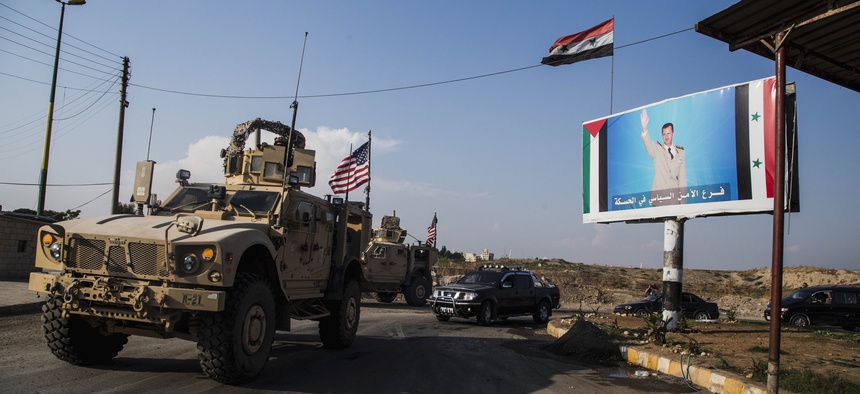 A U.S. military convoy drives through the town of Qamishli, north Syria, by a billboard showing Syrian President Bashar Assad on Saturday, Oct. 26. 2019.