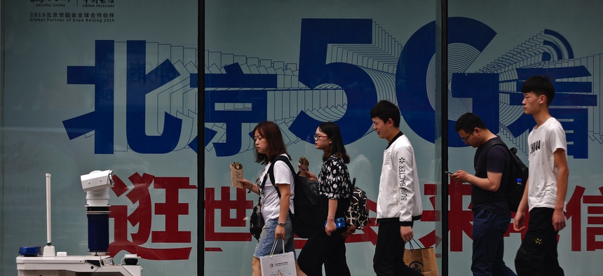 People walk toward a police robot mounted with surveillance cameras patrol past a 5G network advertisement at a shopping district in Beijing, Wednesday, May 15, 2019.