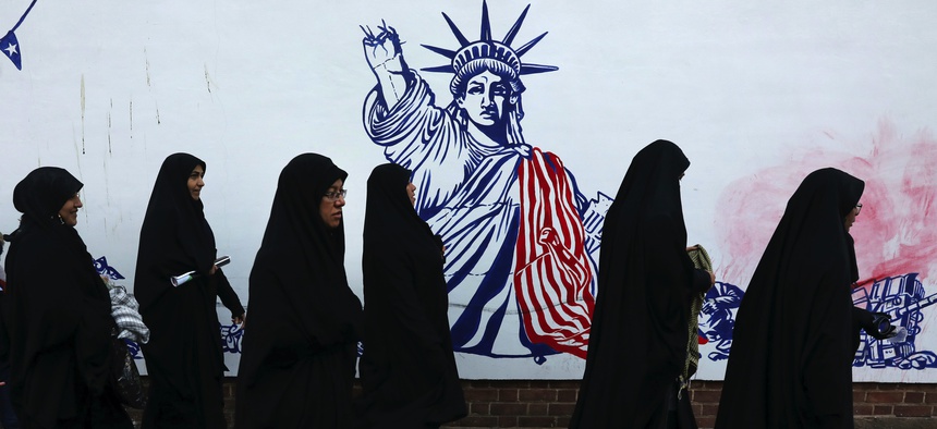 Mourners walk back from a funeral ceremony for Iranian Gen. Qassem Soleimani, passing a satirical drawing of the Statue of Liberty painted on the wall of the former U.S. Embassy in Tehran, Iran, Monday, Jan. 6, 2020.