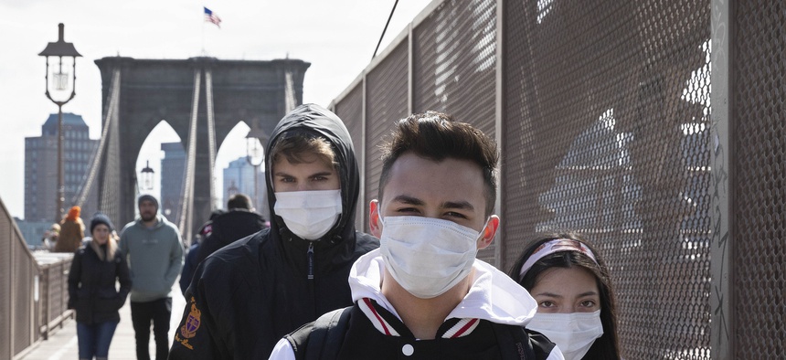 People wear masks as they cross the Brooklyn Bridge, Monday, March 16, 2020 in New York.