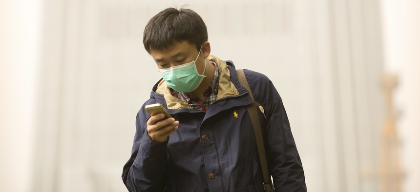 A man wears a face mask as he looks at his mobile phone during a dust and sand storm in Beijing, Thursday, May 4, 2017